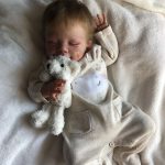 A reborn baby girl peacefully sleeping on a cozy blanket while holding a small stuffed toy.